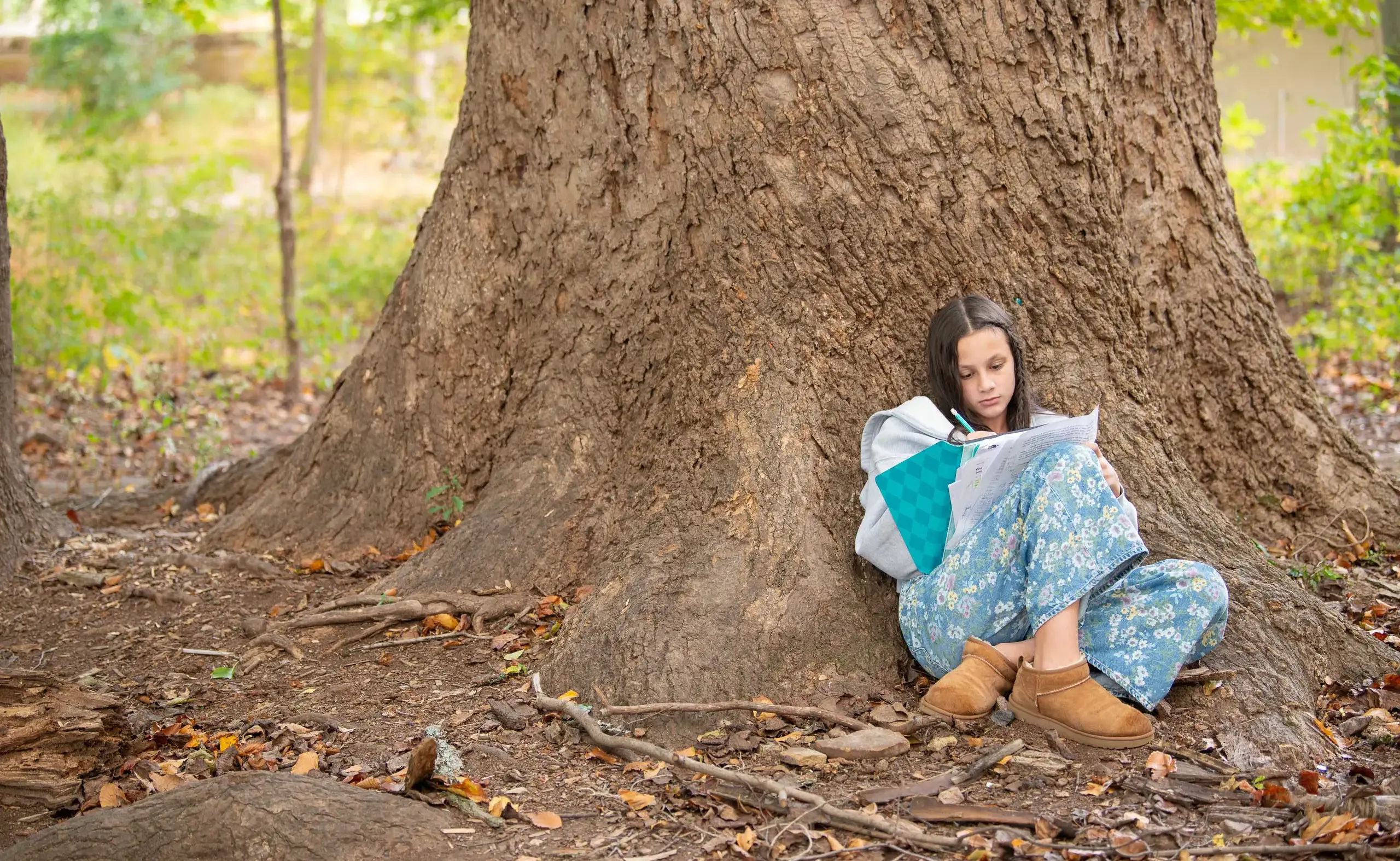 Student writing in notebook under tree