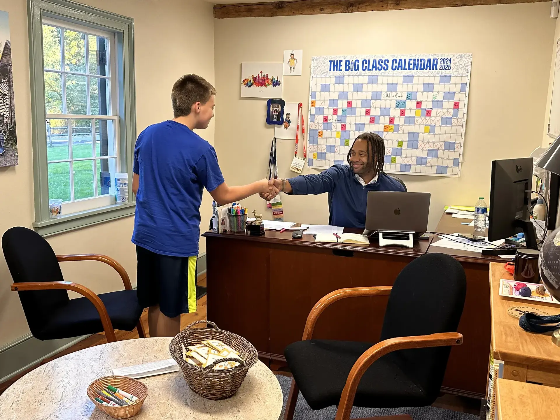 Student and teacher shaking hands across a desk